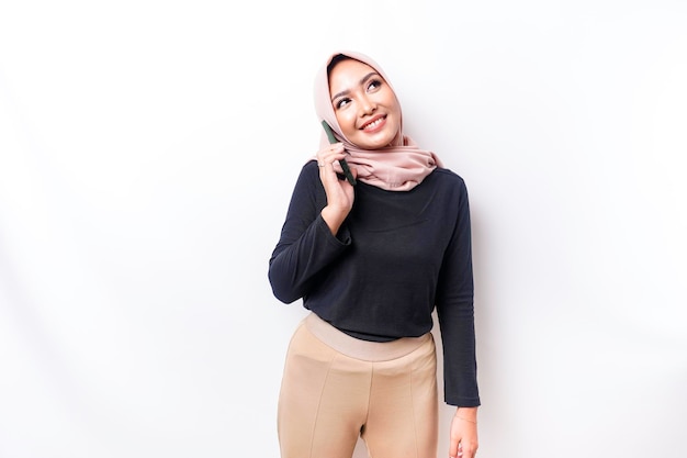 Un portrait d'une femme musulmane asiatique heureuse portant un hijab tenant son téléphone isolé par fond blanc