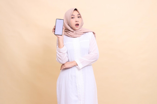 Portrait d'une femme musulmane asiatique portant un hijab en état de choc tenant un gadget de téléphone portable dans sa main avec