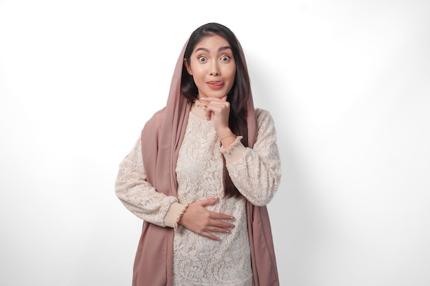 Portrait d'une femme musulmane asiatique portant un voile de foulard mettant les mains sur l'estomac se sentant affamée et voulant manger tout en jeûnant isolée sur un fond blanc concept de Ramadan et Eid Mubarak