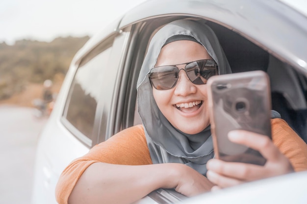 Portrait d'une femme musulmane asiatique souriante en prenant une photo selfie avec un smartphone dans sa voiture