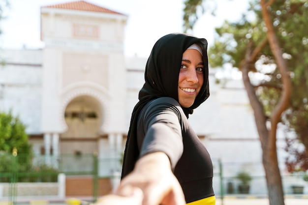 Portrait d'une femme musulmane joyeuse portant un hijab isolé avec fond de mosquée. Vue horizontale de la femme arabe à l'extérieur. Femmes musulmanes, religion et concept d'égalité.