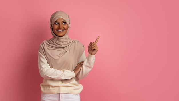 Portrait de femme musulmane souriante en hijab pointant de côté à l'espace de copie