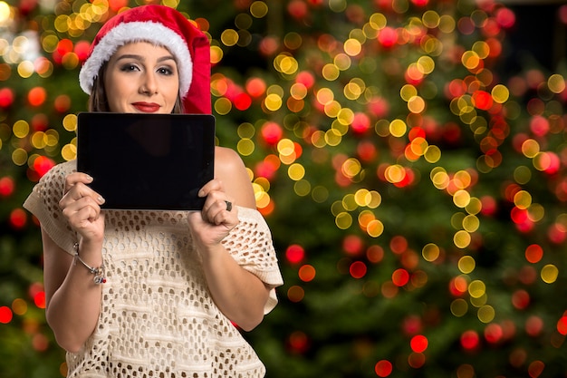 Portrait de femme de Noël tenant la tablette. Femme heureuse souriante sur les lumières de Noël bokeh