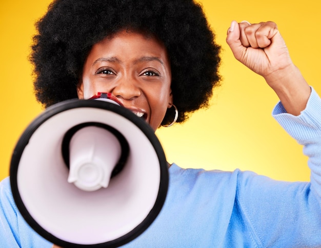 Photo portrait de femme noire et mégaphone avec poing dans un combat de protestation ou une marche sur fond de studio jaune femme africaine ou activiste avec mégaphone sonore ou haut-parleur dans la voix ou la justice