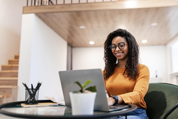 Portrait d'une femme noire souriante utilisant un ordinateur portable à la maison