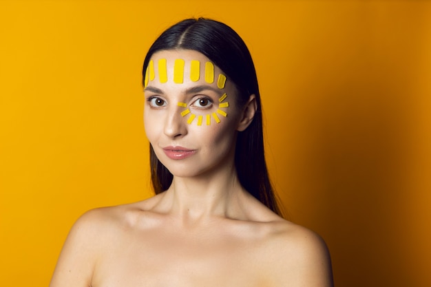 Portrait d'une femme nue sur un mur jaune avec un kinesiotape du visage sur le front