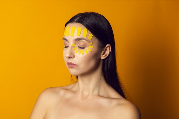 Portrait d'une femme nue sur un mur jaune avec un kinesiotape du visage sur le front