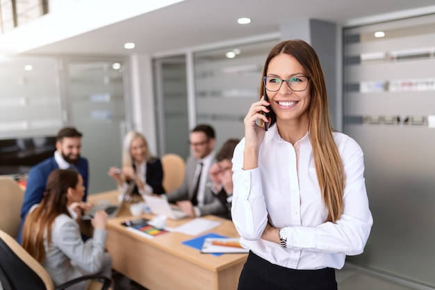 Portrait de femme patron souriant habillé en tenue de soirée et à l'aide de téléphone intelligent tout en se tenant dans la salle du conseil.