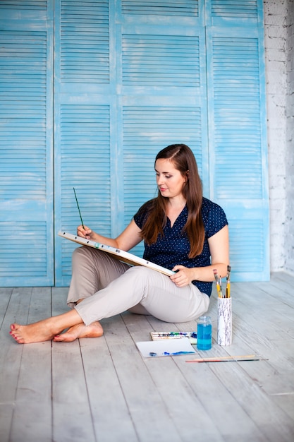 Portrait de femme peintre assis sur le sol près du mur après peinture