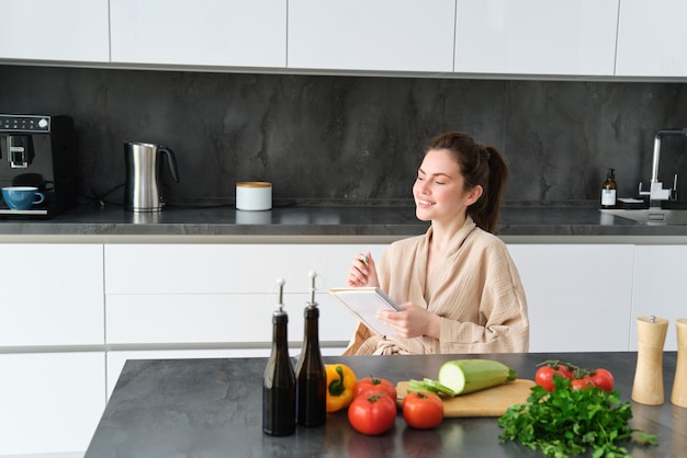 Portrait d'une femme pensant au menu assis dans la cuisine et faisant la liste d'épicerie des légumes et