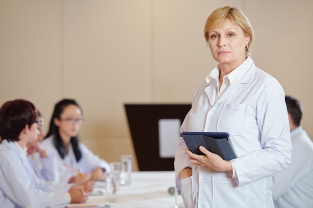 Portrait de femme pharmacologue sérieuse avec ordinateur tablette debout à grande table dans la salle de réunion