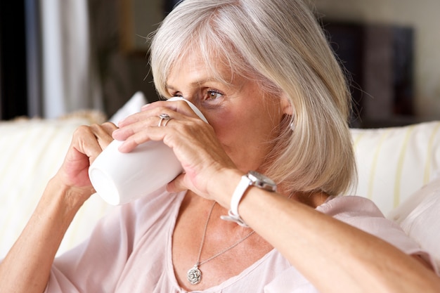 Portrait de femme plus âgée, boire du thé sur un canapé à l&#39;intérieur