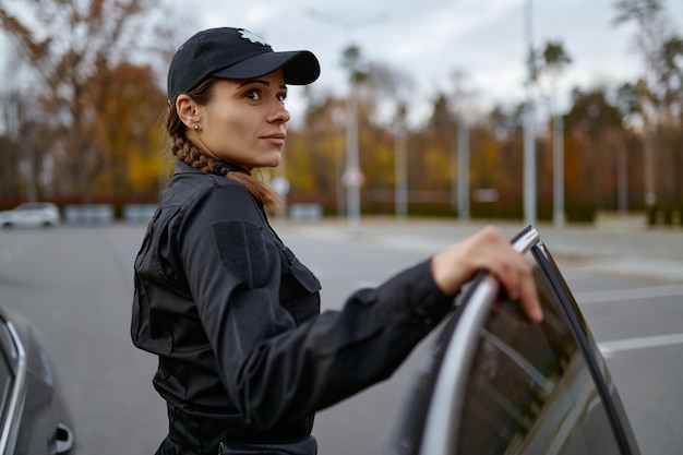 Portrait de femme policière debout près de la voiture sur fond flou. Concept de patrouille, de loi et d'ordre