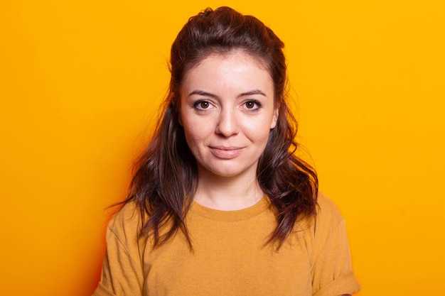 Portrait d'une femme positive debout dans un studio de photographie, regardant la caméra pour poser pour des photos. Personne de race blanche avec un regard joyeux debout sur fond orange isolé.