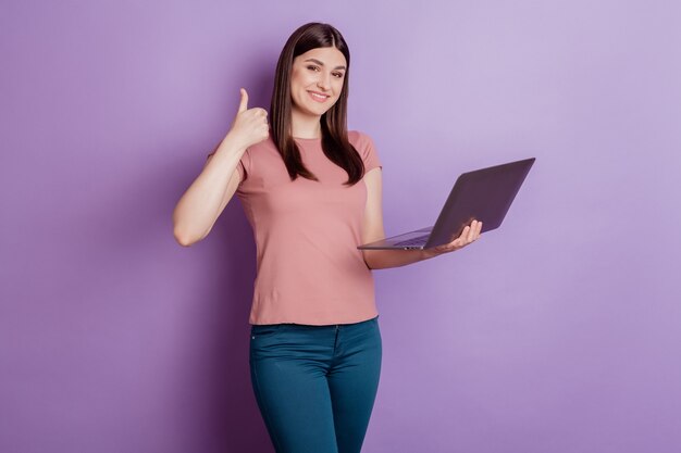 Portrait d'une femme positive et réussie, heureuse, sourire positif, montrer le pouce vers le haut comme utiliser un ordinateur portable isolé sur fond de couleur violette