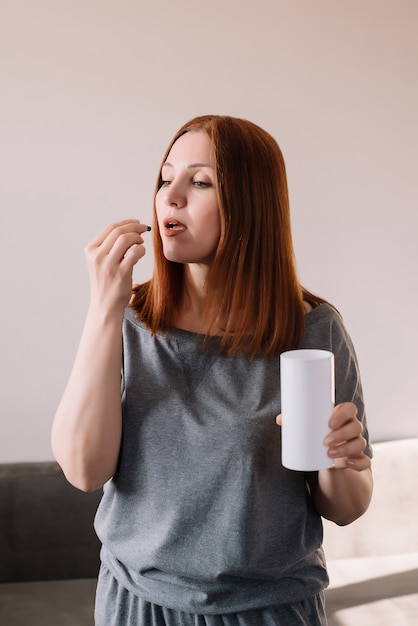 Portrait de femme prend une pilule dans le salon à la maison.