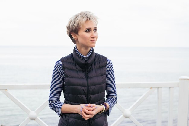 Portrait de femme près de la mer Modèle féminin aux cheveux courts ayant une promenade par temps nuageux Nature concept de temps libre