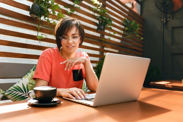 Portrait d'une femme professionnelle mature et confiante assise sur une terrasse d'été au café à l'aide d'un ordinateur portable