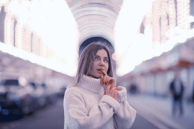 portrait d'une femme pull blanc hiver, saisonnier à l'extérieur de la ville promenade dans la ville du soir