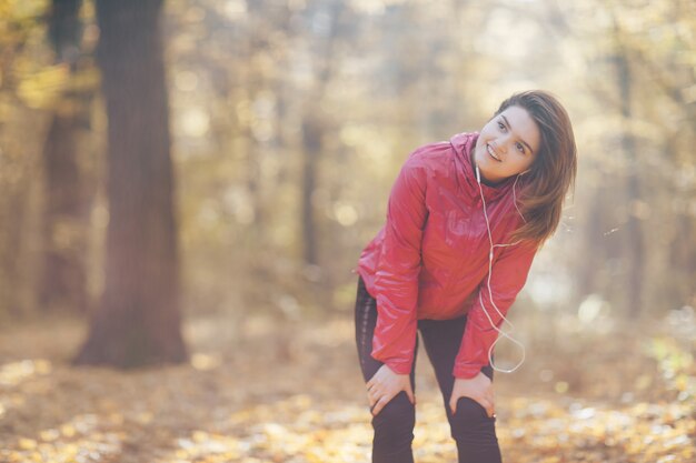 Portrait d'une femme qui s'entraîne et écoute de la musique dans le parc d'automne du matin