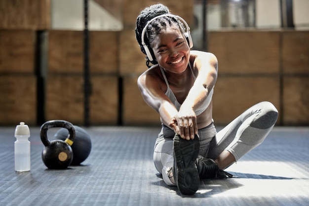 Photo portrait d'une femme qui s'étire avec de la musique au podcast audio de la salle de sport pour la motivation de l'entraînement et heureuse de l'entraînement physique au sol au club de santé athlète africain ou sportif faisant de l'exercice