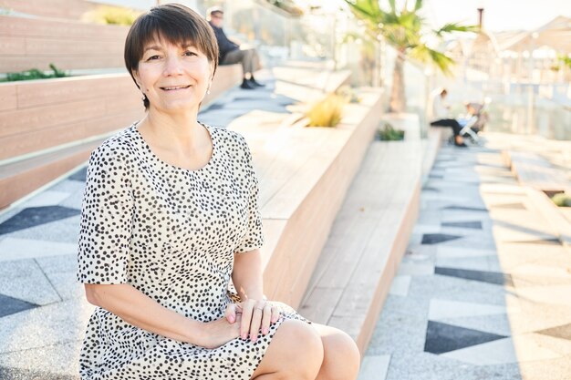 Portrait de femme de race blanche heureuse de 50 ans assis et souriant dans le parc sur le banc, adulte en bonne santé vraie dame