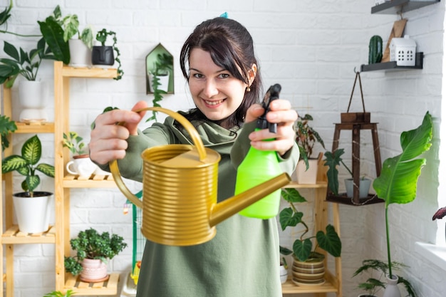 Un portrait d'une femme regarde dans le cadre avec un arrosoir intérieur et un pistolet pulvérisateur pour prendre soin des plantes en pot à la maison