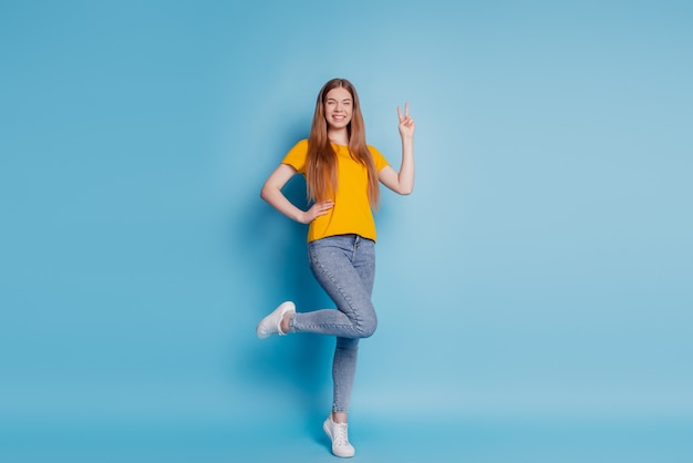 Portrait d'une femme de rêve joyeuse qui montre un signe v portant des vêtements décontractés sur fond bleu