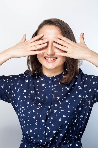 Portrait d'une femme riante fermant les yeux avec les mains sur fond blanc., attendant une surprise