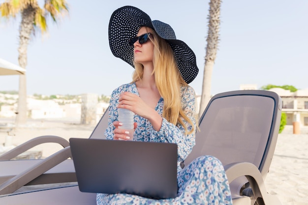 Portrait d'une femme en robe d'été qui travaille sur un ordinateur portable sur la plage