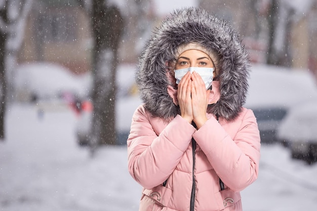 Portrait de femme en rose marchant dans la rue en hiver sous la neige dans un masque de protection pour se protéger contre les maladies infectieuses Protection contre le rhume grippe pollution de l'air Concept de santé