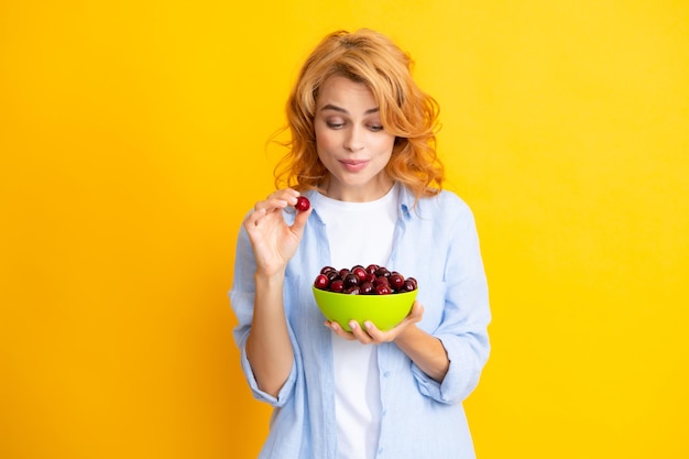 Portrait de femme rougie de beauté avec des cerises sur fond isolé jaune