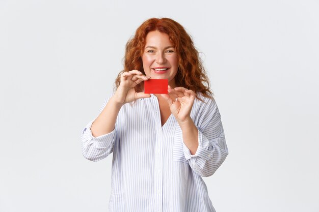 Portrait de femme rousse adulte de 40 ans montrant une carte de crédit avec un sourire heureux.