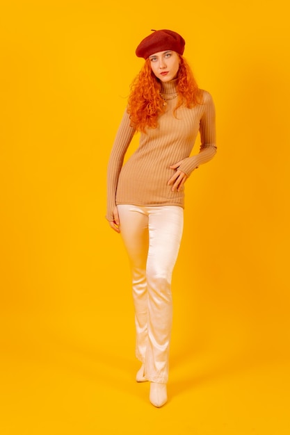 Portrait de femme rousse dans un béret rouge sur fond jaune tourné en studio fashion posé