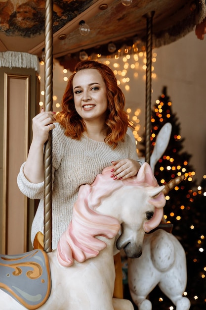 Portrait d'une femme rousse dans un chandail blanc souriant dans le contexte d'un tre de Noël