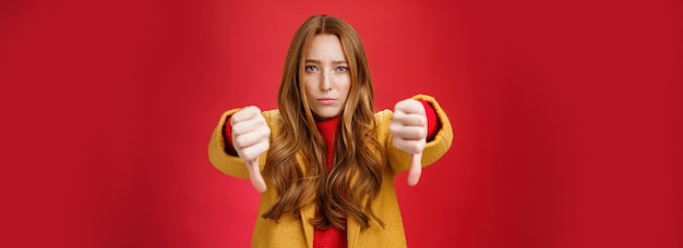 Portrait de femme rousse mignonne peu sûre et peu confiante réagissant à une chose pas cool montrant les pouces vers le bas