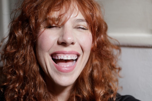 Portrait de femme rousse rire à haute voix à la maison