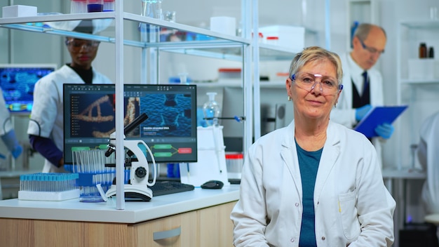 Portrait d'une femme scientifique senior regardant la caméra dans un laboratoire moderne équipé. Équipe multiethnique examinant l'évolution du virus à l'aide d'outils de haute technologie et de chimie pour la recherche scientifique et le développement de vaccins