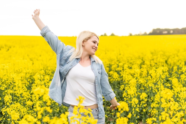 Portrait d'une femme séduisante sur un champ de colza en fleurs avec la lumière du coucher du soleil. Fleurs jaunes et femme heureuse.