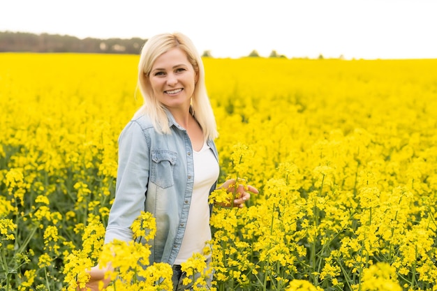 Portrait d'une femme séduisante sur un champ de colza en fleurs avec la lumière du coucher du soleil. Fleurs jaunes et femme heureuse.