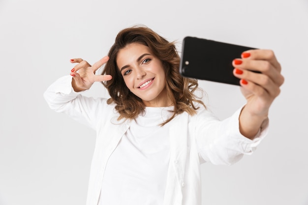 Portrait de femme séduisante dans des vêtements décontractés prenant selfie photo sur téléphone portable, debout isolé