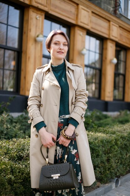 Portrait d'une femme séduisante et élégante, une fille se promène dans la ville à l'extérieur. Image moderne et féminine élégante, style. Fille dans un manteau ou un manteau beige et une robe verte