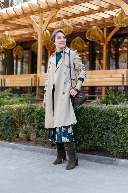 Portrait d'une femme séduisante et élégante, une fille se promène dans la ville à l'extérieur. Image moderne et féminine élégante, style. Fille dans un manteau ou un manteau beige et une robe verte