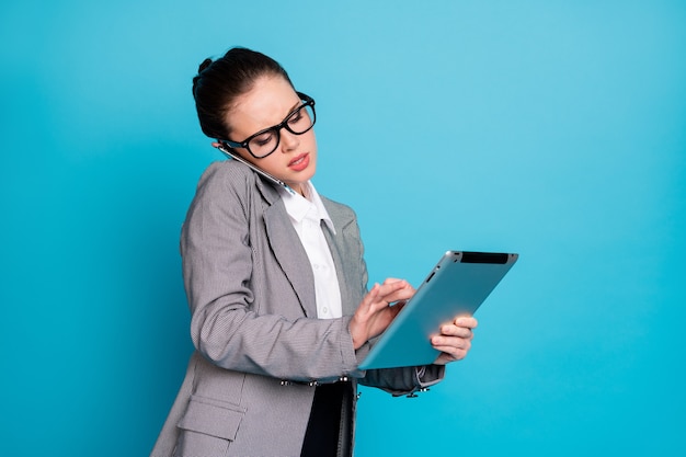 Portrait d'une femme séduisante et occupée qui appelle le client à l'aide d'un appareil isolé sur un fond de couleur bleu vif