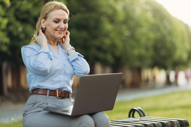 Portrait femme senior active avec ordinateur portable dans le parc travaillant à l'extérieur