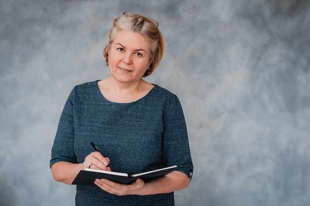 Portrait d'une femme senior belle entreprise sur un mur gris