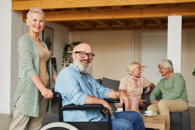 Portrait de femme senior avec homme handicapé en fauteuil roulant souriant à la caméra avec d'autres personnes