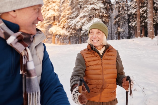 Portrait d'une femme senior souriante marchant avec des poteaux dans la forêt d'hiver avec son mari