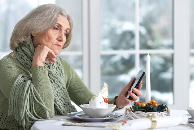 Portrait de femme senior triste assis à table avec téléphone