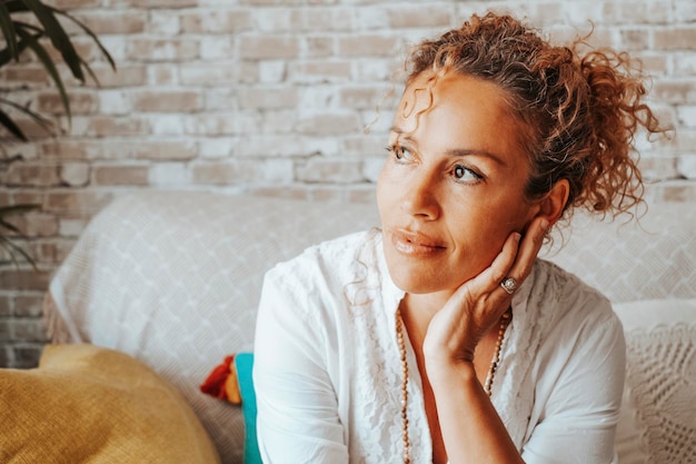 Portrait d'une femme sereine regardant par la fenêtre à la maison ayant du temps de détente assis sur le canapé Vue de face de femmes heureuses et confiantes Attrayant d'âge moyen pensant heureux intérieur